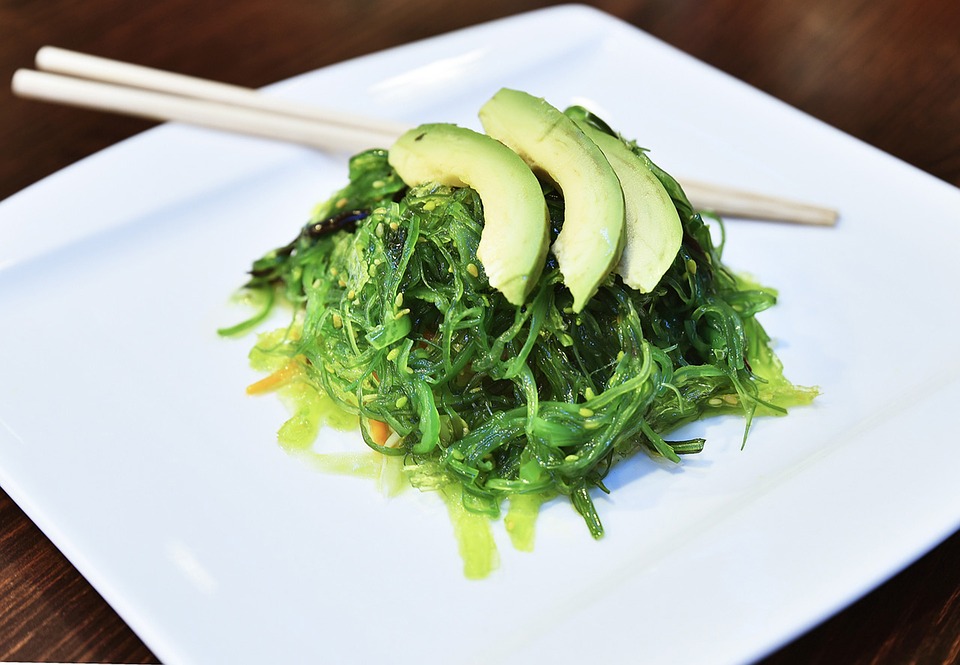 Seaweed salad topped with avocado on a white plate