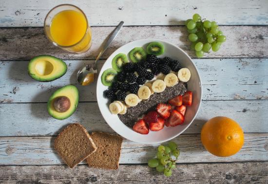 Bowl of fruit, grapes, oranges, avocado, bread slices, and a glass of orange juice on a table