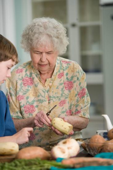 An older woman is peeling potatoes in the kitchen with a male adolescent.