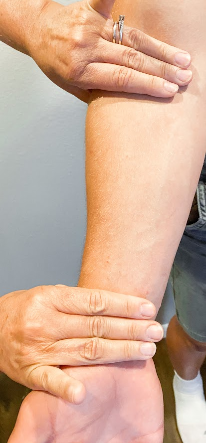 Photo showing closeup of patient's arm with nurses fingers placed at wrist and elbow.