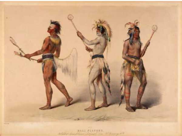 Three men in tribal clothing standing next to each other, two facing the left and the third facing the right. They wear paint, hold game sticks, and wear headdresses.