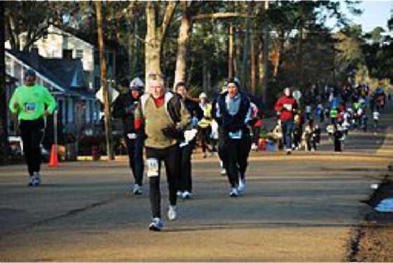 People running on the road for a marathon. A house, trees, and cones are in the background.