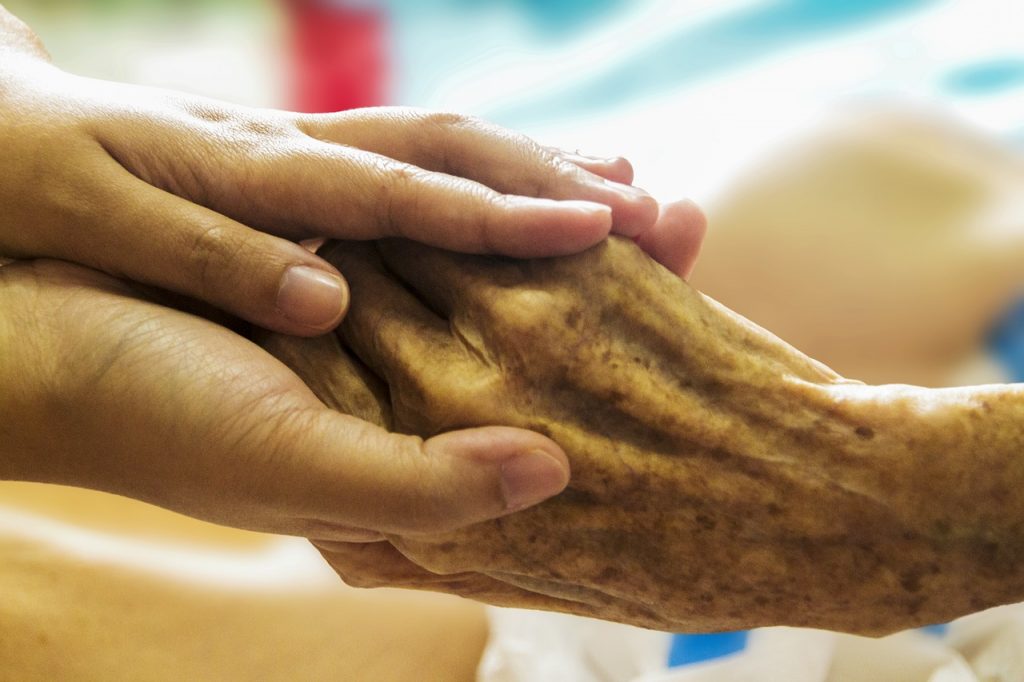 Photo showing closeup of a younger hand holding an elderly one