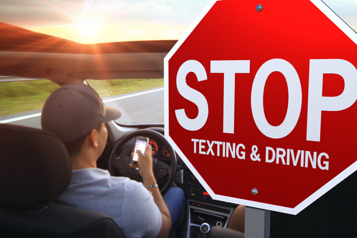 תמונה המציגה את נהג הרכב מסתכל על הטלפון הסלולרי עם הודעות עצירה גדולות ושלט נהיגה לצידם