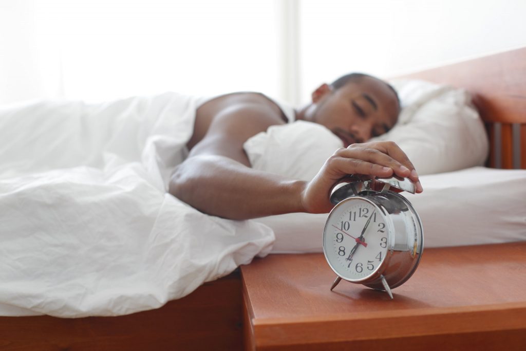 Image showing a person reaching out from a bed to shut off an alarm clock on side table