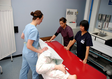 Imagen que muestra a tres miembros del personal médico posicionando a un paciente en un tablero deslizante