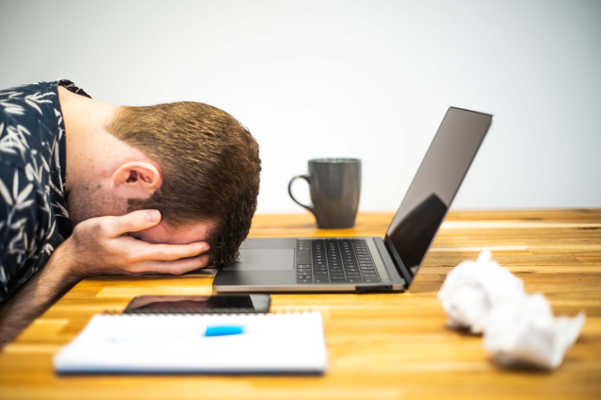 Photo showing a person with head on table, hands holding head, office supplies and laptop on table