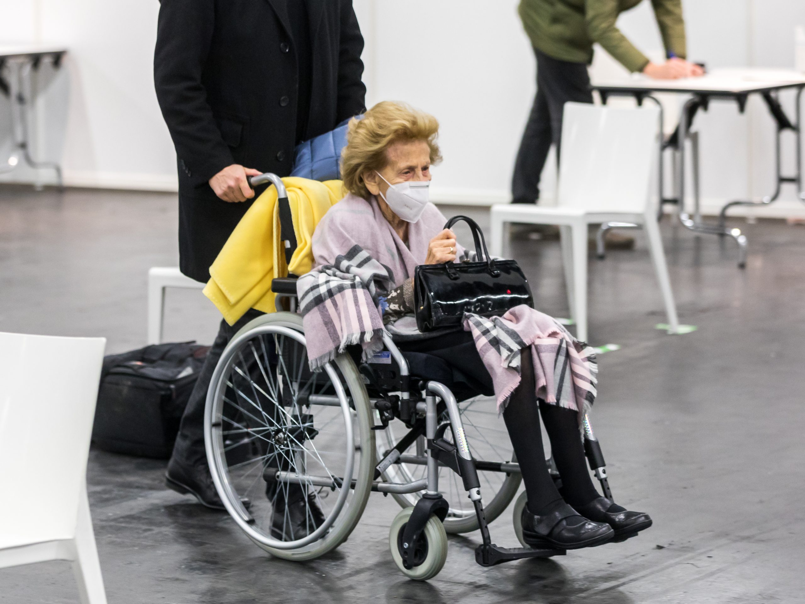 Foto que muestra a una anciana, con máscara siendo empujada en silla de ruedas