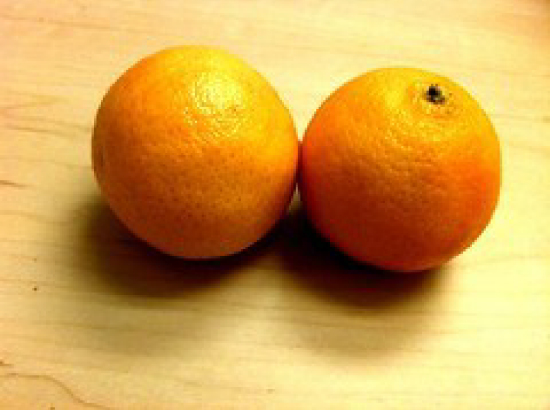 Two whole oranges placed side by side on a light wooden surface.