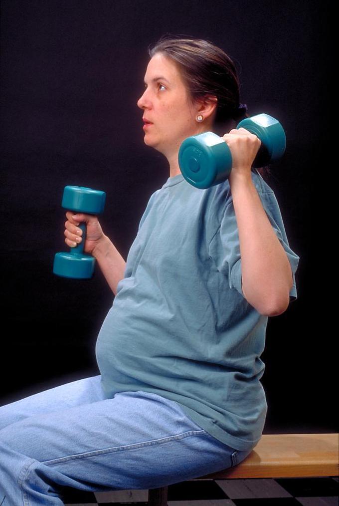 This is a photograph of a pregnant woman in gym clothes lifting hand weights. A strong, healthy woman will generally have a good pregnancy outcome. Physicians recommend moderate exercise during pregnancy, including strength-training.