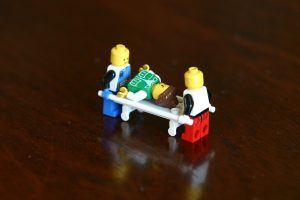 Two Lego figures moving a third Lego figure on a stretcher