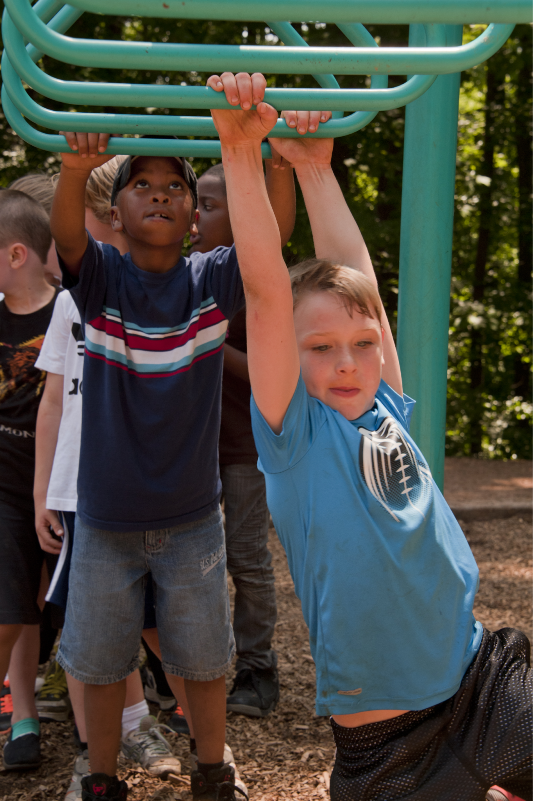 Photo of children playing on a set of horizontal bars on a playground.
