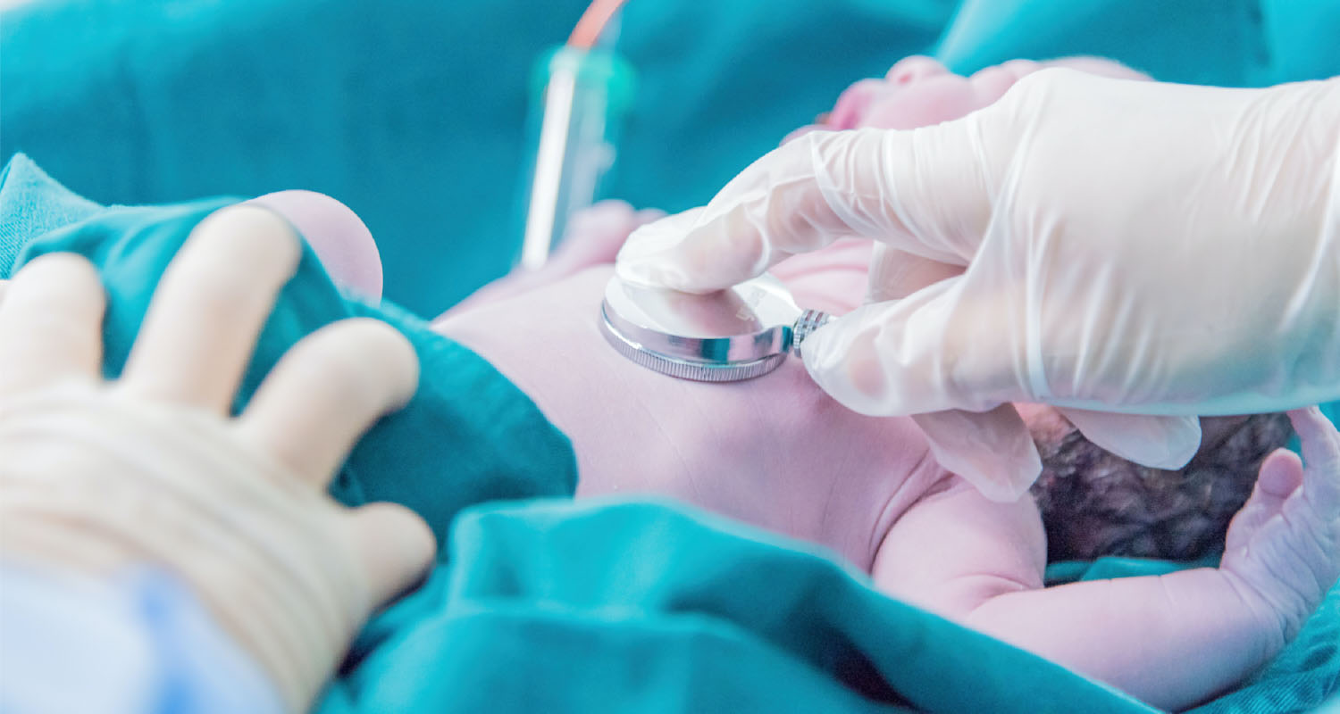 Photo of newborn infant with a stethoscope on its chest amid blue blankets.