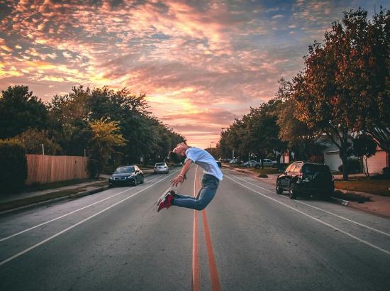 A man jumping high and touching his heels in the air during a susnset with colored clouds.