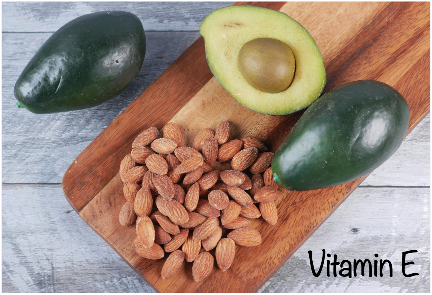 Avocados and almonds displayed on a wooden cutting board, with text labeling "Vitamin E".