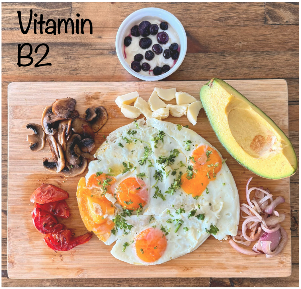 Breakfast spread on a wooden board featuring eggs, mushrooms, tomatoes, avocado, cheese, and a small bowl of yogurt with berries.