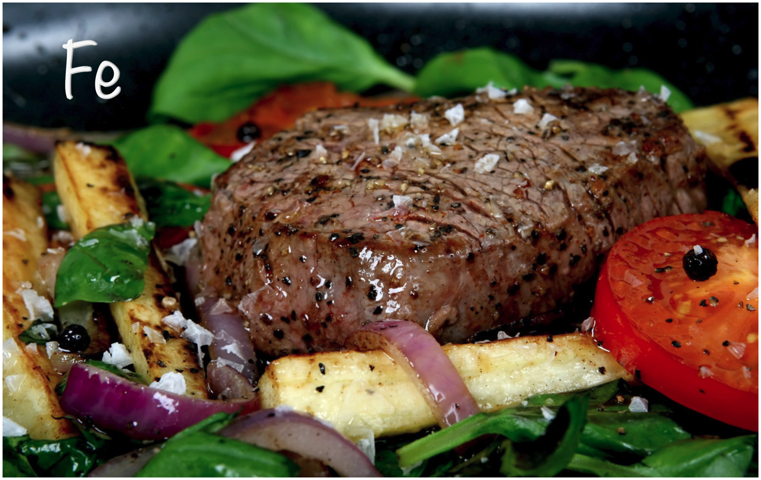 A perfectly cooked steak on a bed of greens, with roasted vegetables and sliced tomatoes, garnished with salt.